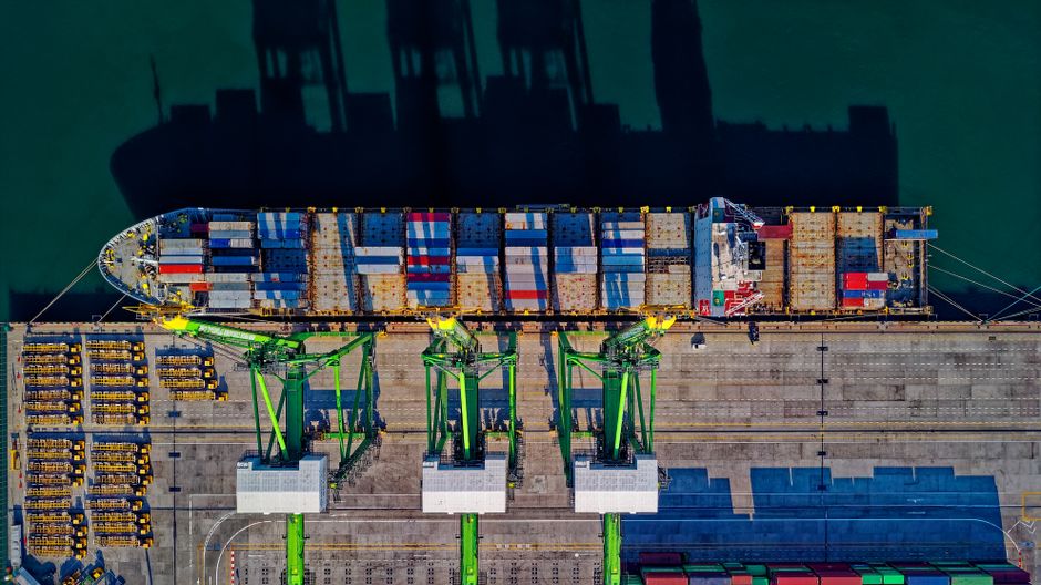 Aerial view of a large cargo ship at a bustling port, illustrating the global maritime trade that the Strait of Hormuz disruption threatens.