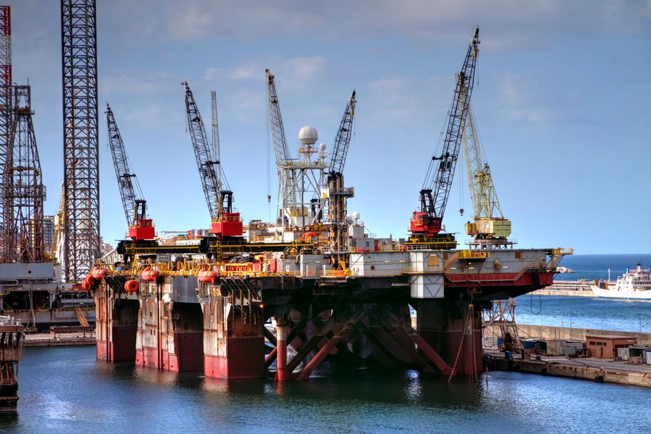 Offshore oil platform with cranes over harbor water, representing energy infrastructure exposed to maritime risk