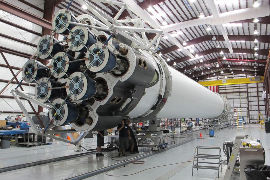 A rocket core under construction at a modern aerospace factory, photographed from a low angle.