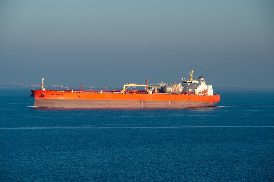 Large orange LNG carrier ship cruising through calm sea waters on a clear day.