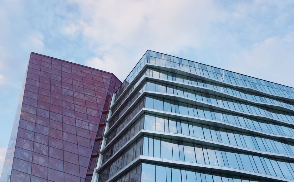 Contemporary high-rise building with glass and red facade against a blue sky.